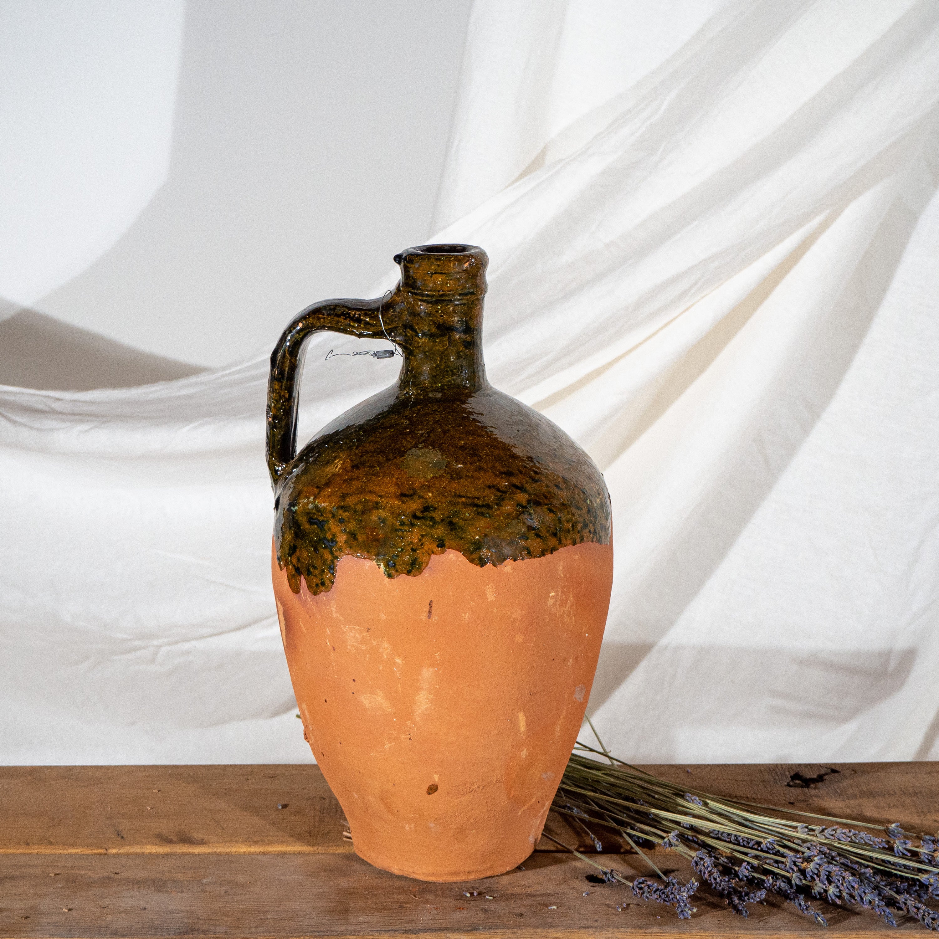 Single handled glazed terracotta Turkish jug with spout on vintage wooden bench with dried lavendar