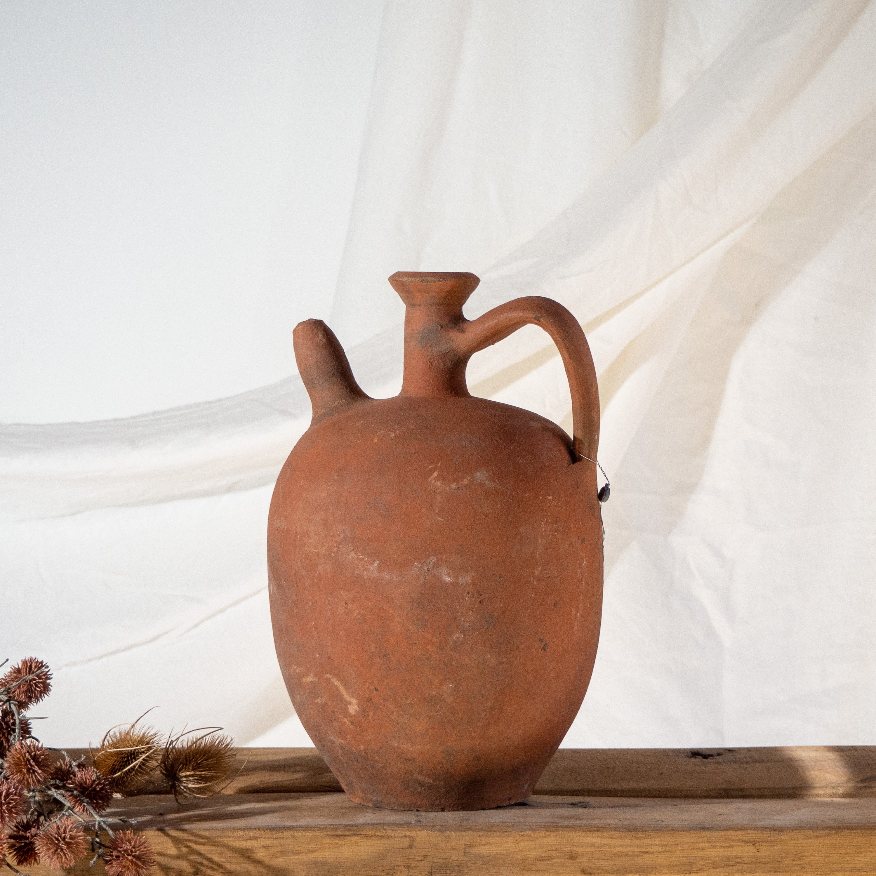Vintage Turkish terracotta jar with spout and single handle on vintage timber bench seat with dried flowers