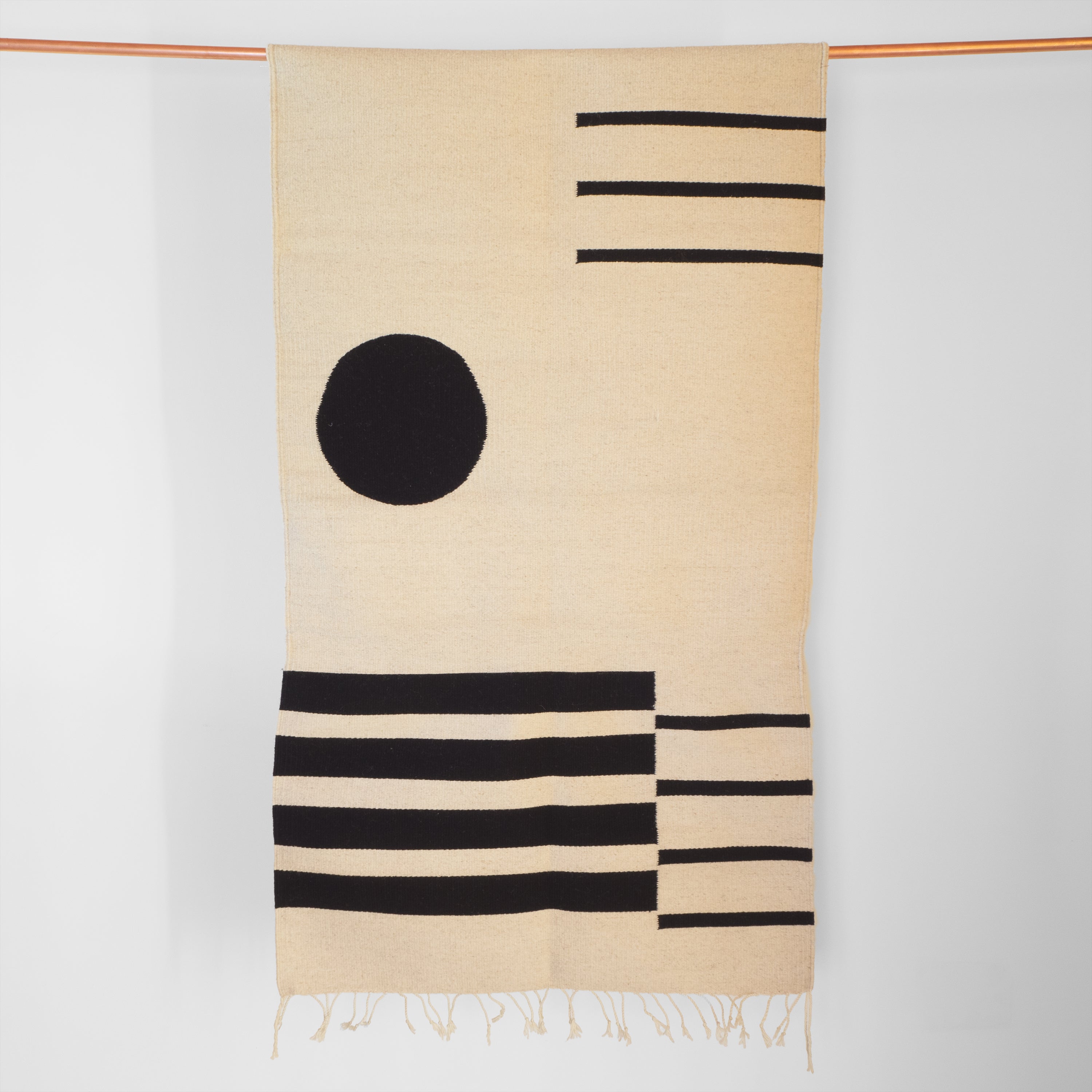 Handwoven cream and black sheep&#39;s wool accent rug from women&#39;s cooperative in Mexico hanging on copper pipe