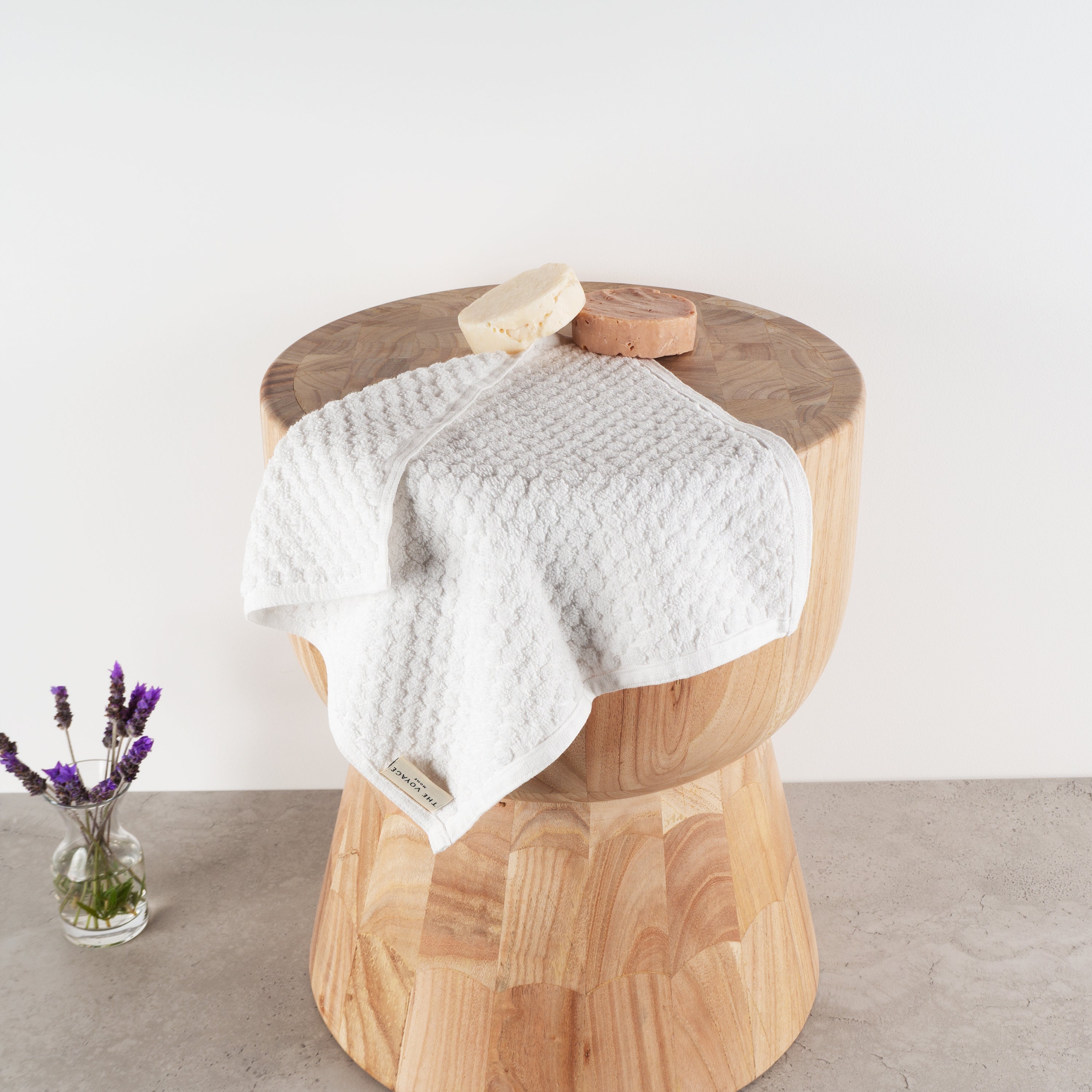 Handwoven white GOTS certified organic cotton Turkish loop face towel draped over wooden stump on grey tiles with soap and lavender
