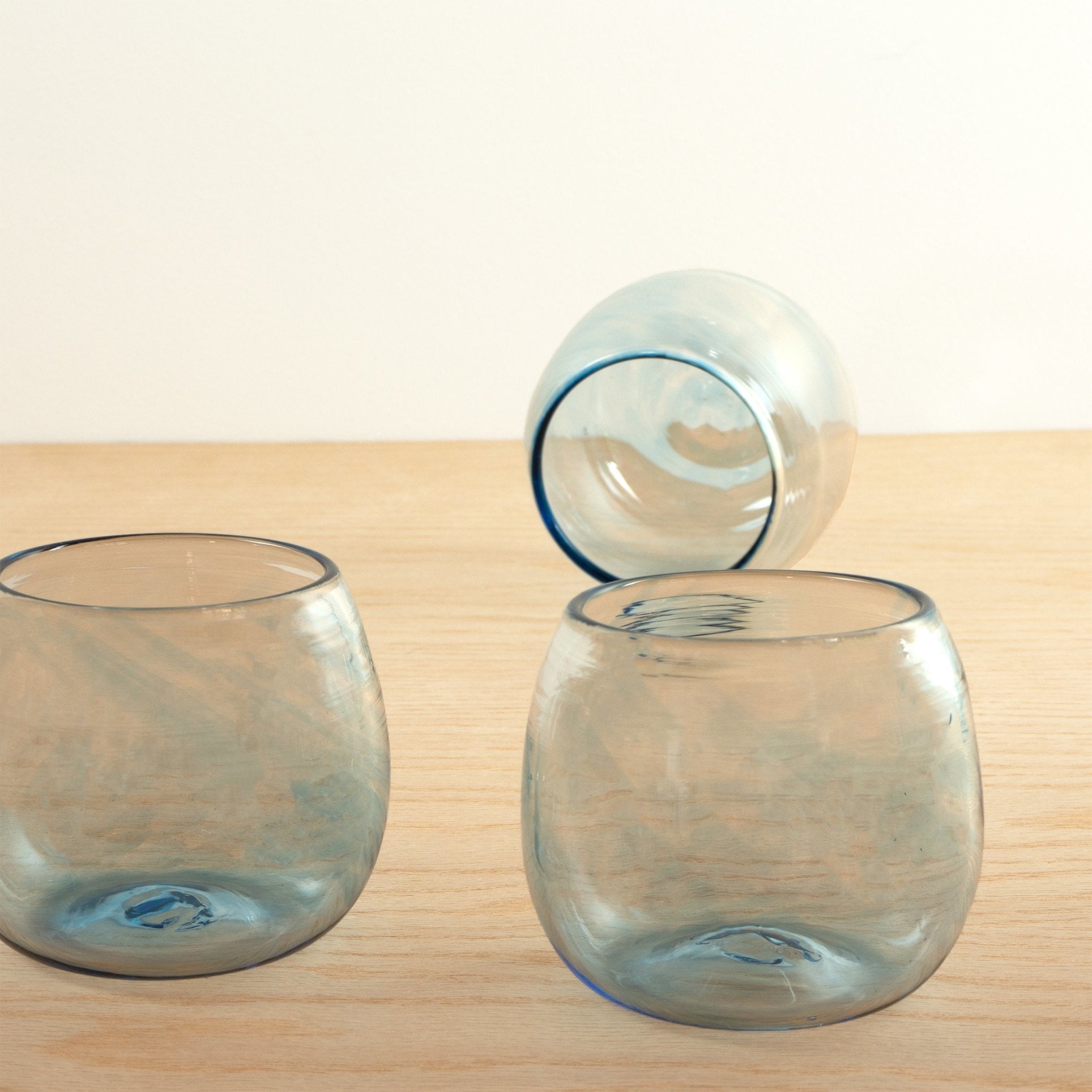 Three blue handblown round glasses from Oaxaca, Mexico arranged on a wooden table