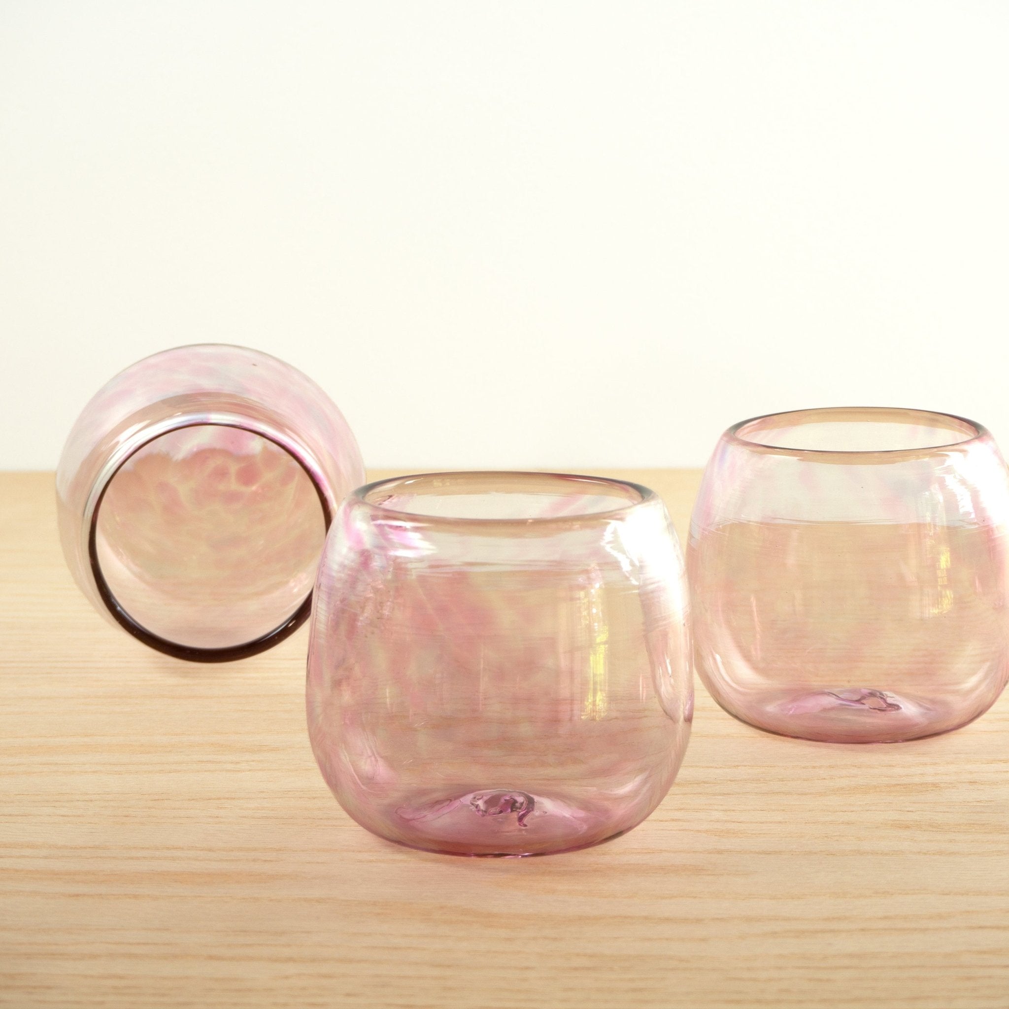 Three handblown round pink glasses arranged on a wooden table