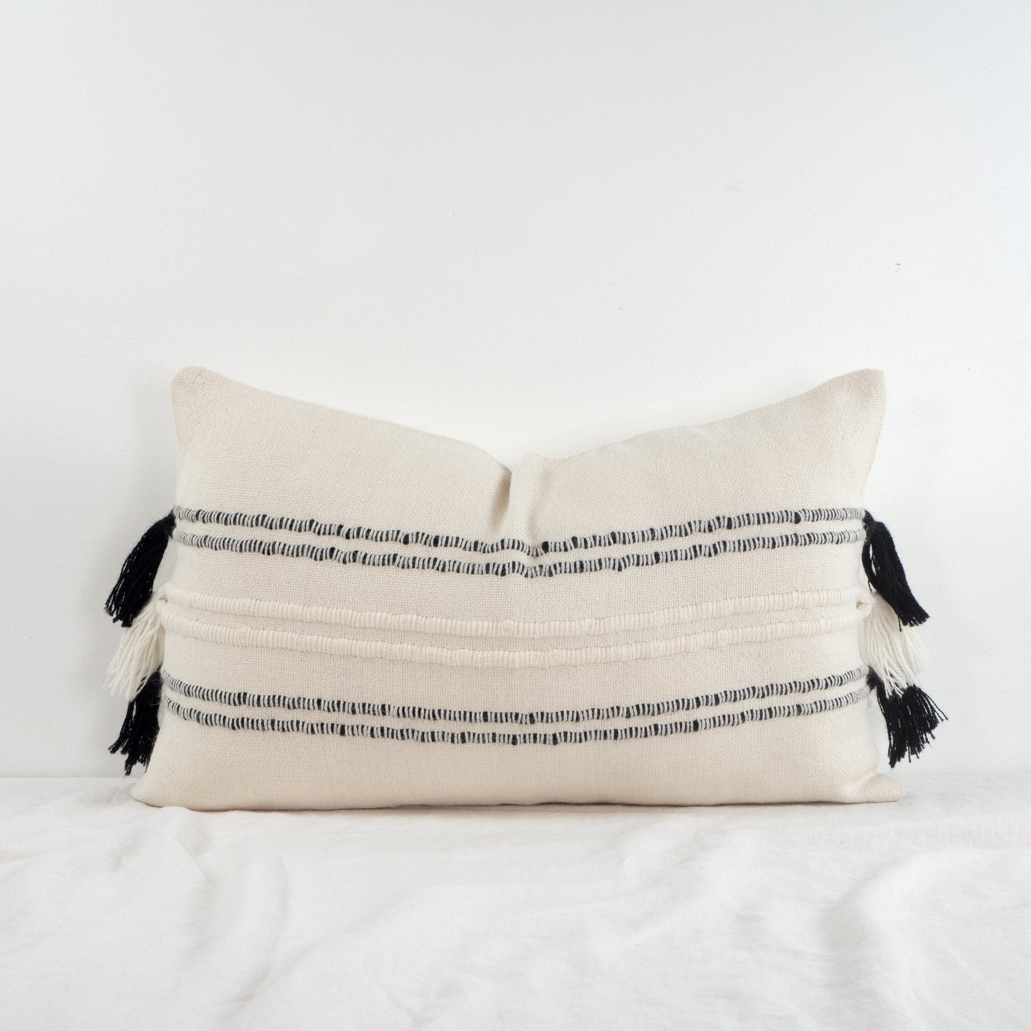 Handwoven white and black baby alpaca lumbar cushion from Peru on a table