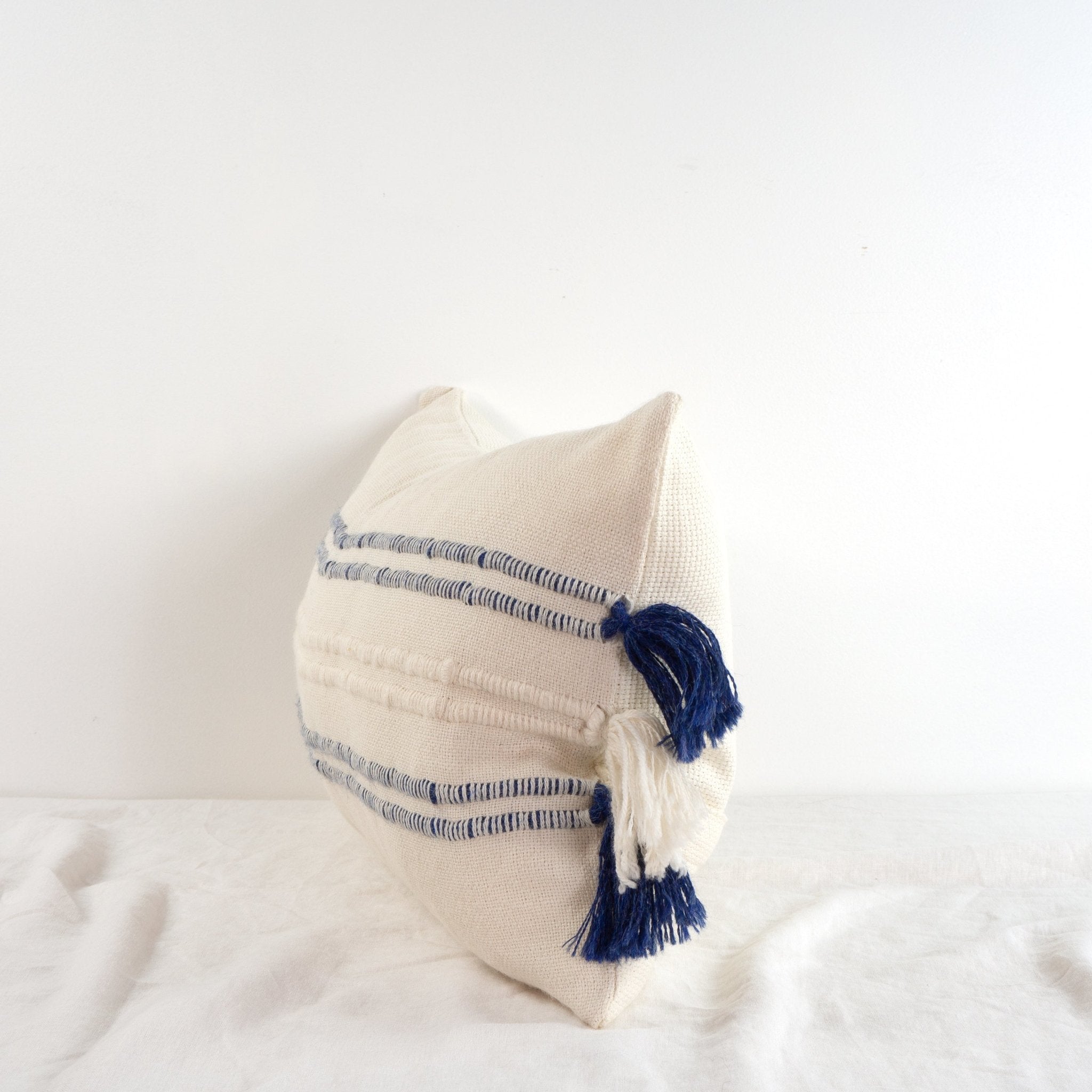 Handwoven white and navy blue baby alpaca lumbar cushion from Peru on a table side on