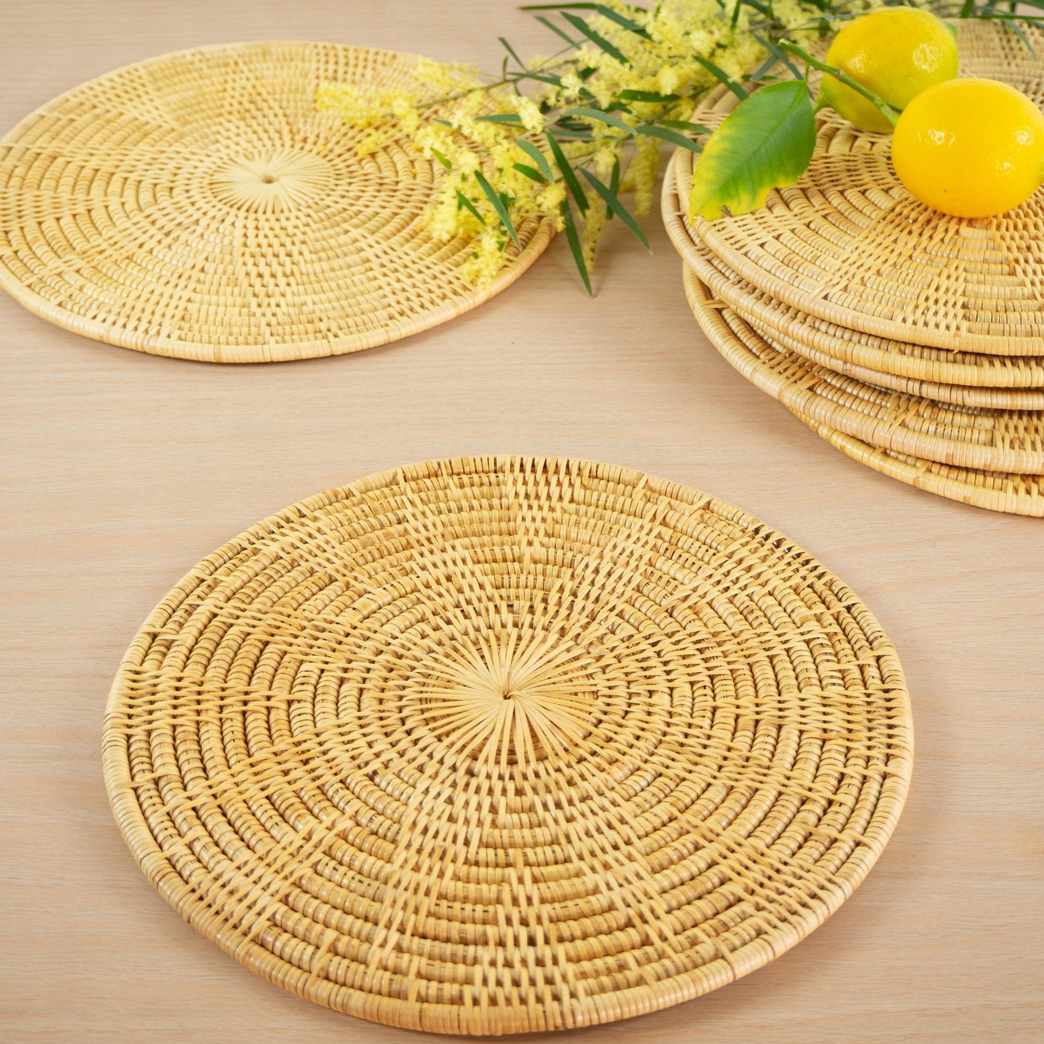 Eight round rattan handwoven artisan placemats from Cambodia on wooden table with lemons and Australian native wattle